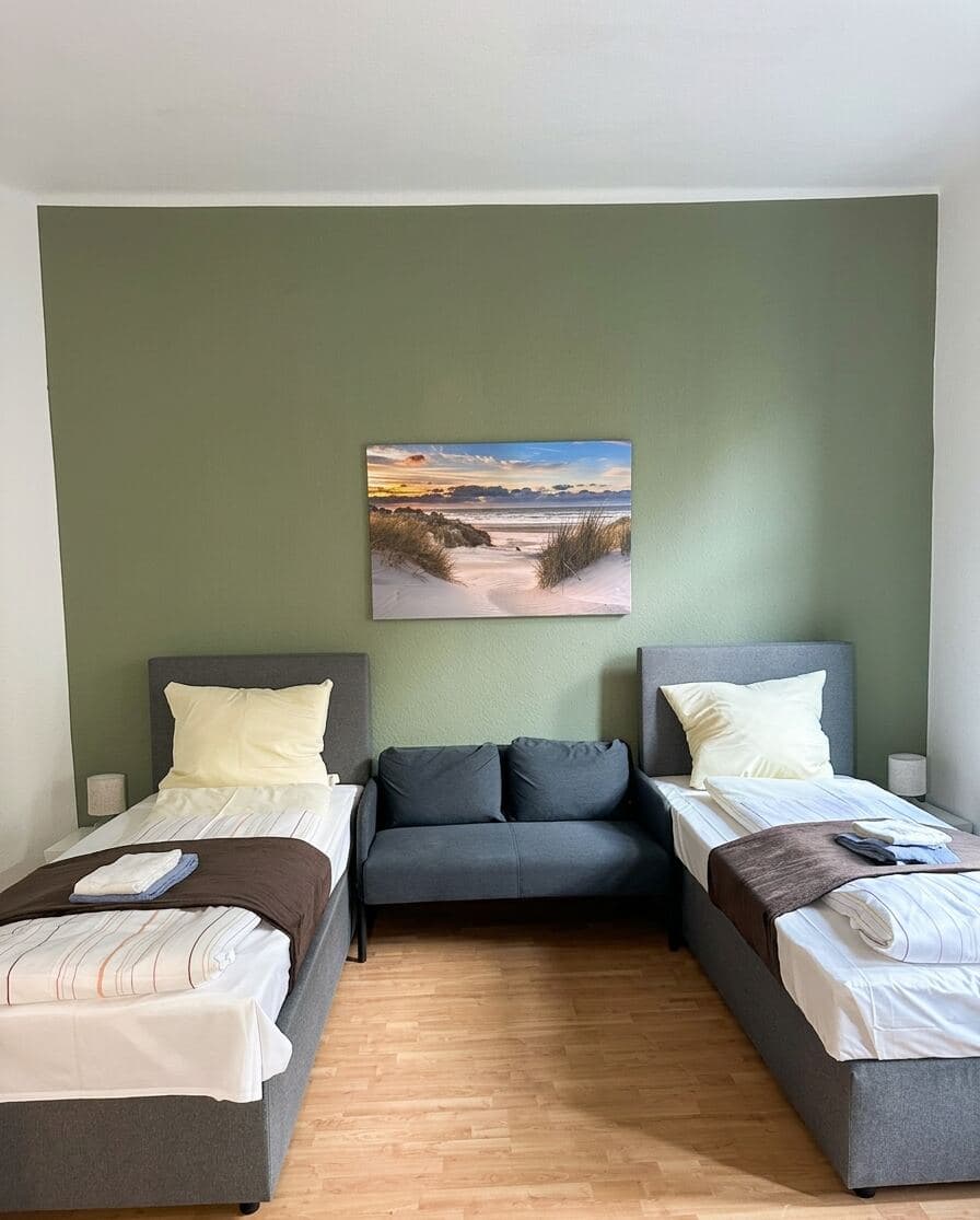 Apartment mit grüner Akzentwand, zwei Betten und einer Sitzgruppe